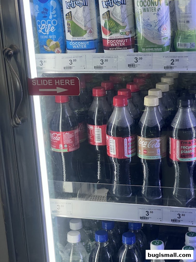 A refrigerated display case filled with various bottled drinks, including Coca-Cola and coconut water.