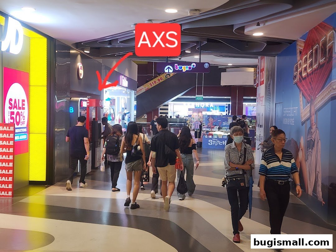 People walking past shops in a mall, with a prominent AXS Station sign.